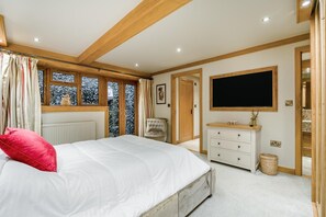 A bedroom with a bed, a dresser, a television, and a window with curtains.