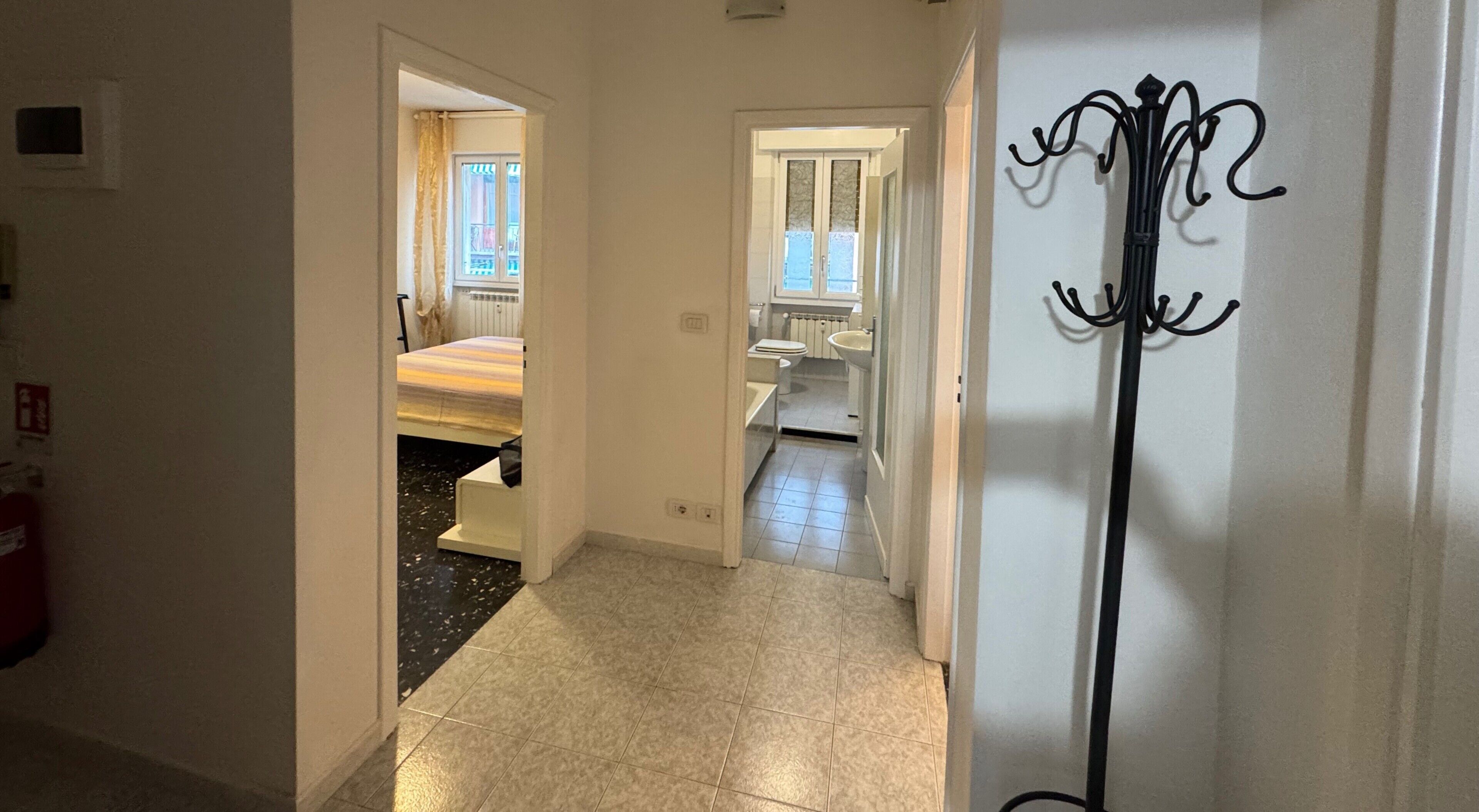 A hallway leading to a bedroom with a bed, a bathroom with a toilet and sink, and a coat rack.