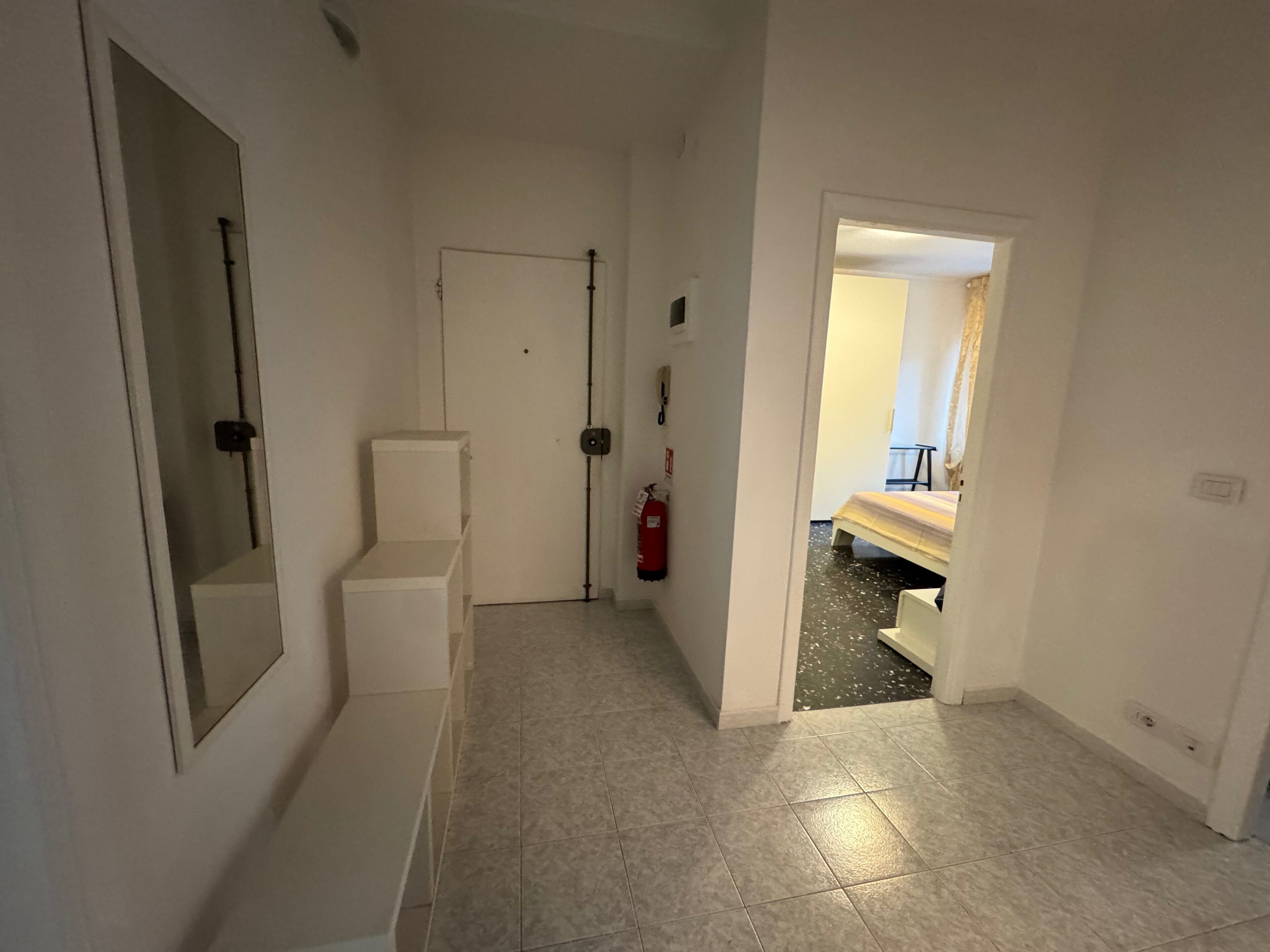 Un couloir avec une porte blanche, un extincteur et un escalier.