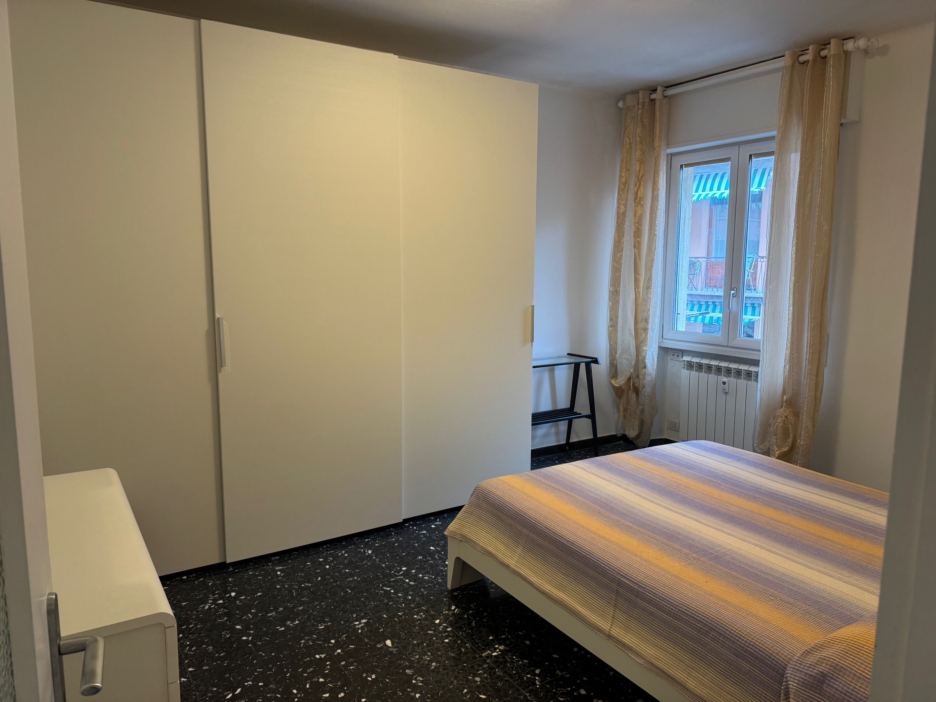 Une chambre à coucher avec un lit, une armoire, un radiateur et une fenêtre avec des rideaux.