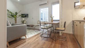 Ein gemütlicher Wohnbereich mit Sofa, Esstisch, Stühlen, einer Topfpflanze und einer Küchenzeile.