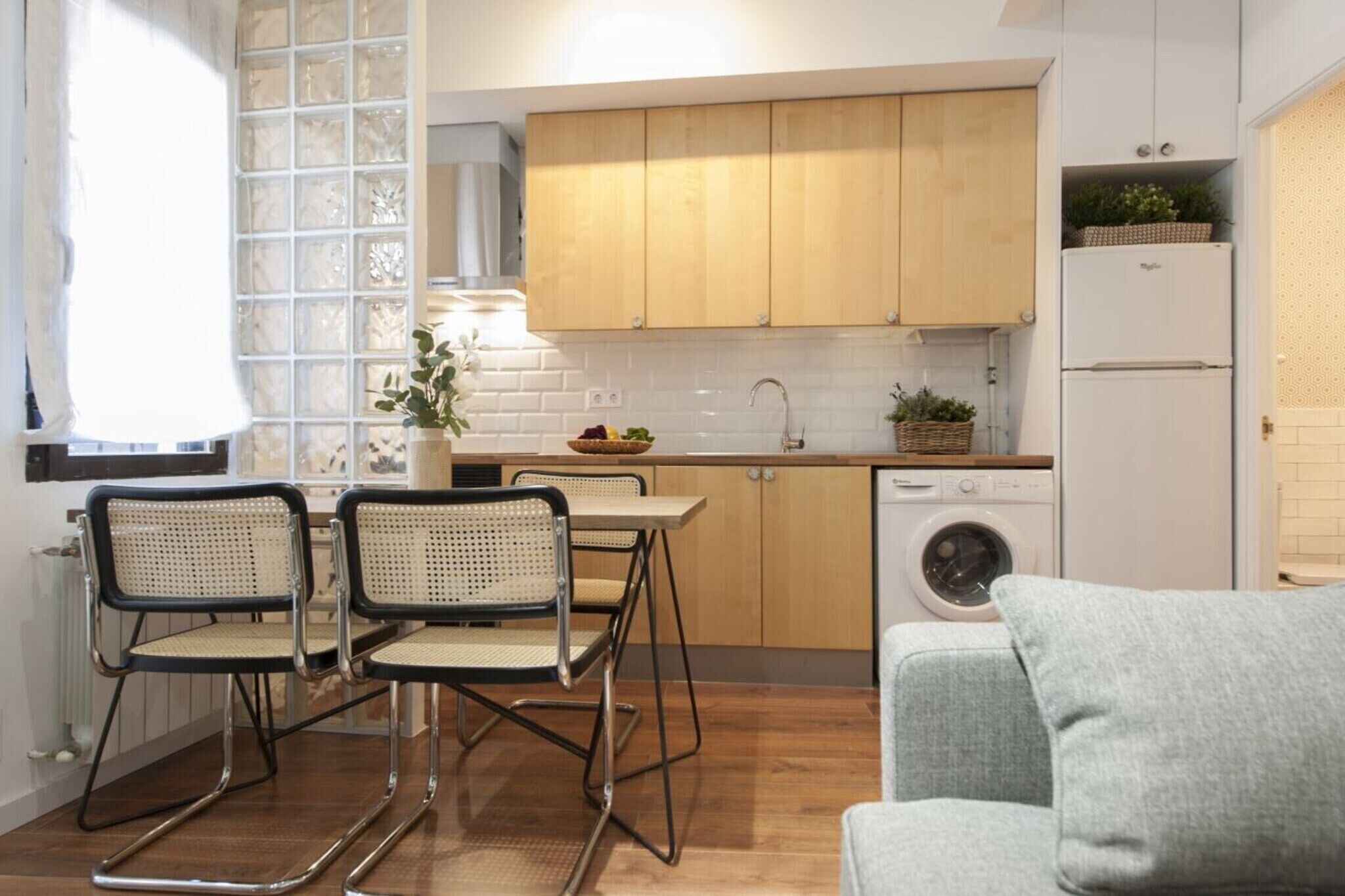A compact kitchen with wooden cabinets, a washing machine, and a dining area with two chairs.