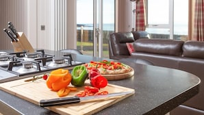 Een keuken met een gasfornuis, een snijplank met groenten, en een pizza op het aanrecht.