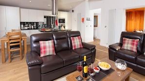 Een moderne woonkamer met een bruine leren bank, een houten salontafel met wijnglazen, een fles wijn en snacks.