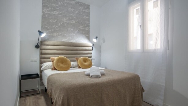 Une chambre à coucher avec un lit, des lampes de chevet, une fenêtre et un mur décoré d’un motif.