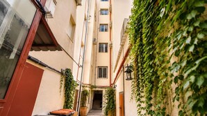 Une ruelle étroite, avec un immeuble recouvert de lierre d’un côté, une porte de l’autre, et un escalier menant à un étage supérieur.
