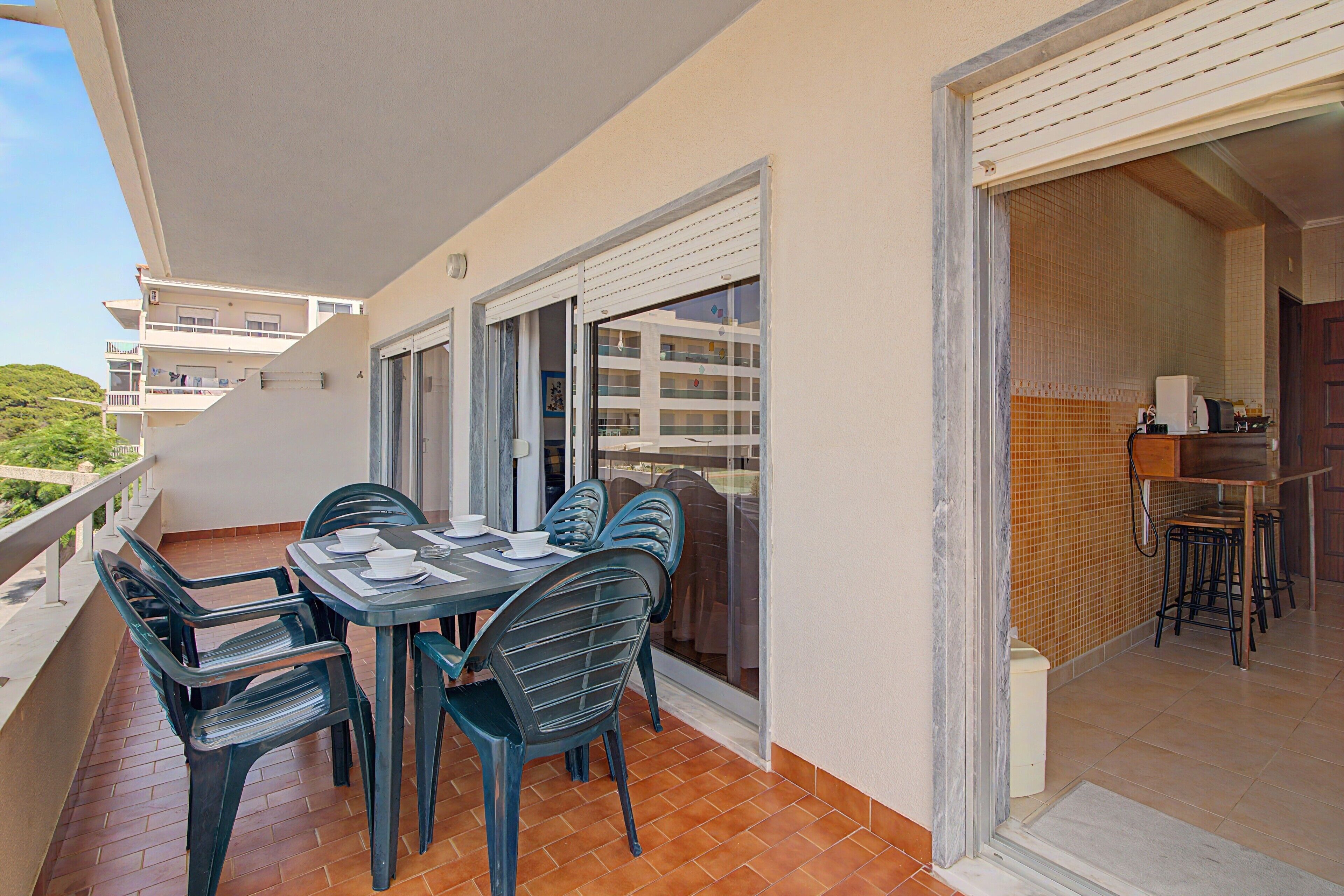 A balcony with a table set for dining, chairs, and a view of a building with balconies.