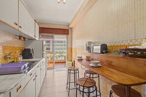 A compact kitchen with a wooden countertop, a coffee maker, and a toaster. There are stools at the bar counter. - Apartment 'Estrela Do Forte' with Shared Pool, Balcony and Wi-Fi (Quarteira)