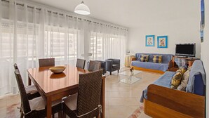 En moderne stue med spiseplads, sofasæt, et fjernsyn og kunst på væggen.
