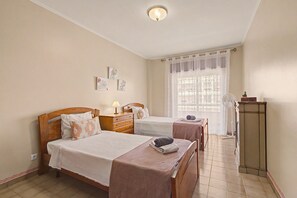 Ein Hotelzimmer mit zwei Betten, einem Nachttisch mit Lampe, einem Fenster mit Vorhang und einer Heizung.