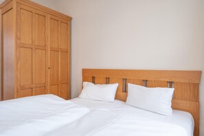 A bed with a wooden headboard, white bedding, and a wooden wardrobe. - Schone Ferienwohnung mit Balkon und Ganzjahrigem Ahoi-rabatt (Sellin)
