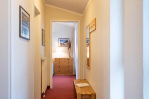 Ein schmaler Flur mit einer hölzernen Bank, einem Heizkörper, einer Kommode aus Holz und gerahmten Bildern an den Wänden.