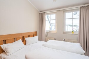 Habitación de hotel con dos camas, cabecero de madera, ventana con cortinas y un radiador.