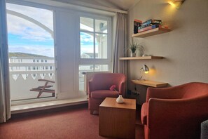 A room with a large window, a red armchair, a wooden side table, and a shelf with books. - Schone Ferienwohnung mit Balkon und Ganzjahrigem Ahoi-rabatt (Sellin)