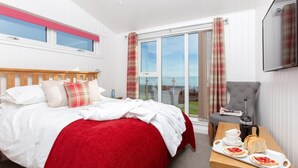 Ein Hotelzimmer mit einem Bett, einem Tisch mit Frühstücksgebäck und -speisen, einem Sessel und einem Fernseher.