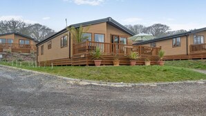 A row of wooden cabins with balconies, a gravel driveway, and a grassy area with potted plants. - 2 Bed in Upton (oc-c35149) (Ryde)