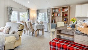 A cozy room with a dining table, chairs, a sofa, a red plaid ottoman, a bookshelf, and a welcome sign. - 2 Bed in Upton (oc-c35149) (Ryde)