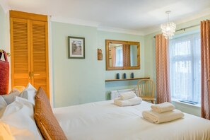 Ein Schlafzimmer mit Bett, Sessel, Heizkörper, Spiegel und einem Fenster mit Vorhängen.