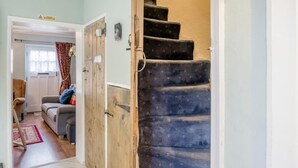 Een trap met een houten leuning en beklede treden, leidend naar een kamer met een bank en een deur.