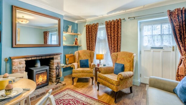 Een knusse woonkamer met een open haard, twee fauteuils, een bank en een eettafel, plus een grote spiegel.
