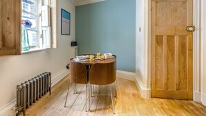 Una habitación con piso de madera, una mesa redonda con sillas, un radiador, una ventana con vista y una puerta.