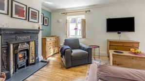Una sala de estar con chimenea, un sillón gris, un televisor y un aparador de madera.
