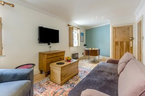 Ein Wohnzimmer mit Fernseher, Holzmöbeln, einem Esstisch und einer Couch.