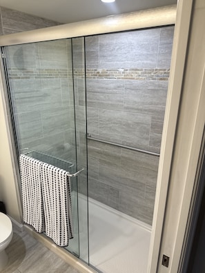 A glass-enclosed shower with grey tiles, a towel rack, and a toilet visible to the left. - Luxurious Minimal 19th-Floor Highrise [Waterview] (Fort Myers)