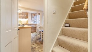 Eine Treppe führt zu einer zweiten Etage, ein Küchenbereich mit Esstisch und Stühlen sowie eine Tür zu einem weiteren Raum.