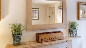 Ein Spiegel mit Holzrahmen, eine Holzkiste mit dem Schriftzug 'BOLLINGER' und zwei Blumentöpfe auf einem Kaminbrett.