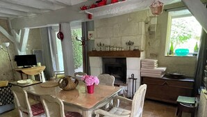 A rustic dining area with a wooden table, wicker chairs, a fireplace, and a television on a stand. - Charming Vacation Rental in Touraine (Chançay)