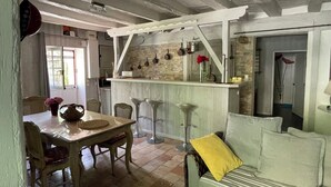 A rustic kitchen with a wooden table, bar stools, and a bar counter. - Charming Vacation Rental in Touraine (Chançay)