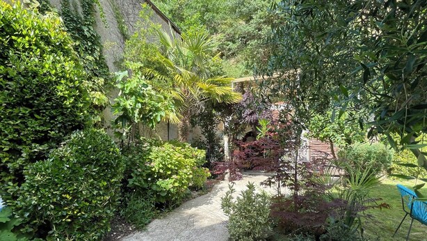 A garden pathway surrounded by dense foliage and a small structure in the background. - Charming Vacation Rental in Touraine (Chançay)