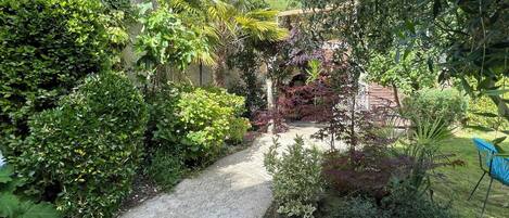 Un sentier de jardin bordé d’une végétation luxuriante, avec une petite construction visible au fond.