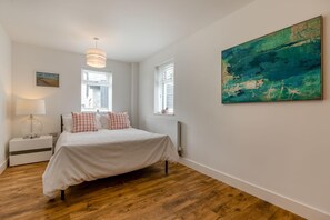 Une chambre à coucher avec un lit, des tables de chevet, une lampe, une fenêtre et un tableau.