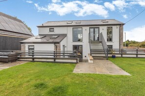 A modern two-story house with a covered patio, a staircase leading to the upper floor, and a fenced yard.