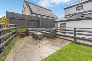 A patio with a sectional sofa and a coffee table, surrounded by a wooden fence and a stone pathway.