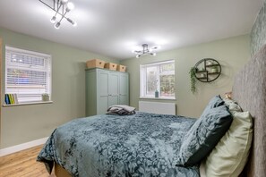 A bedroom with a bed, two windows, a wardrobe, and a ceiling light fixture.