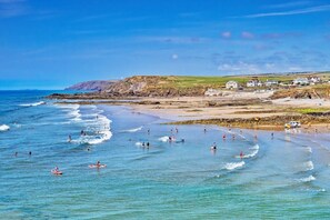 A coastal beach scene with waves, people, and houses in the background. - 3 Bed in Sheepwash (oc-b35145) (Sheepwash)