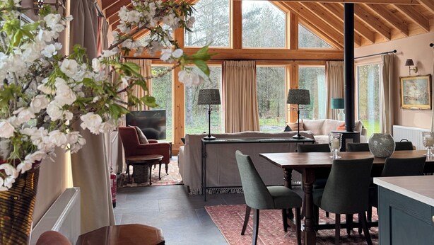 Ein geräumiges Zimmer mit hohen Decken, Holzbalken, einem Essbereich und großen Fenstern.