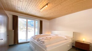Una camera da letto con un letto grande, una testiera in legno, un comodino con una lampada e vista sulle montagne dalla finestra.