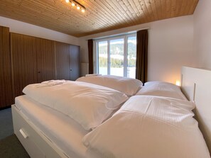 A bedroom with a large bed, wooden wardrobe, and a window with a view of a snowy landscape. - Haus Montana 3/7 Appartement/Fewo,   5-Bettwohnung by Interhome (Lenzerheide)