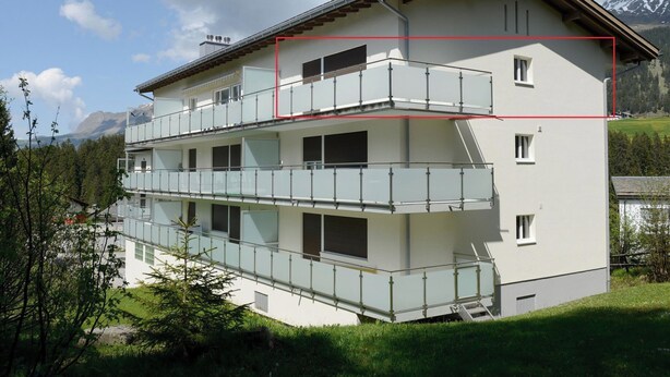 Un edificio a più piani con balconi, una scala e montagne sullo sfondo.