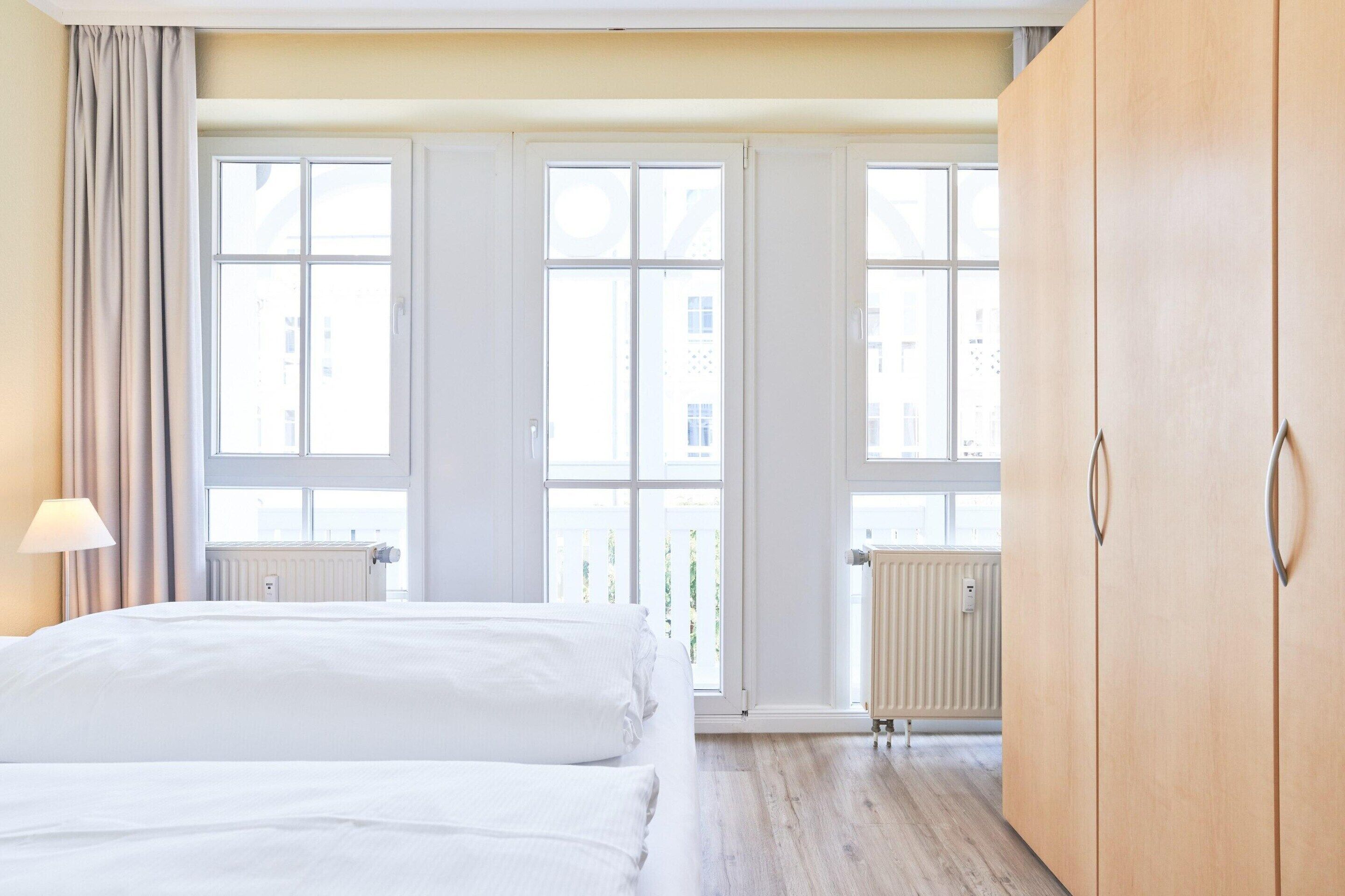 Une chambre d’hôtel avec un lit, une armoire en bois et de grandes fenêtres.