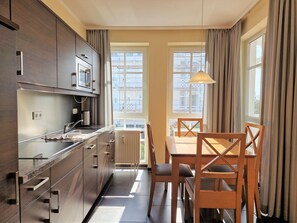 Eine moderne Küche mit Edelstahlgeräten, einem Essbereich mit Holzkästen und großen Fenstern mit Vorhängen.