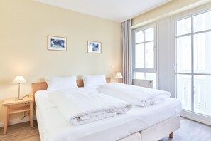 Ein Hotelzimmer mit einem großen Bett, zwei Nachttischen, einem Fenster und zwei gerahmten Bildern an der Wand.