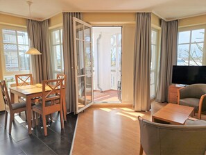 A room with a dining table, chairs, a sofa, a TV, and a sliding glass door leading to an outdoor area. - Moderne Ferienwohnung mit Grossem Balkon im Seepark Sellin (Sellin)