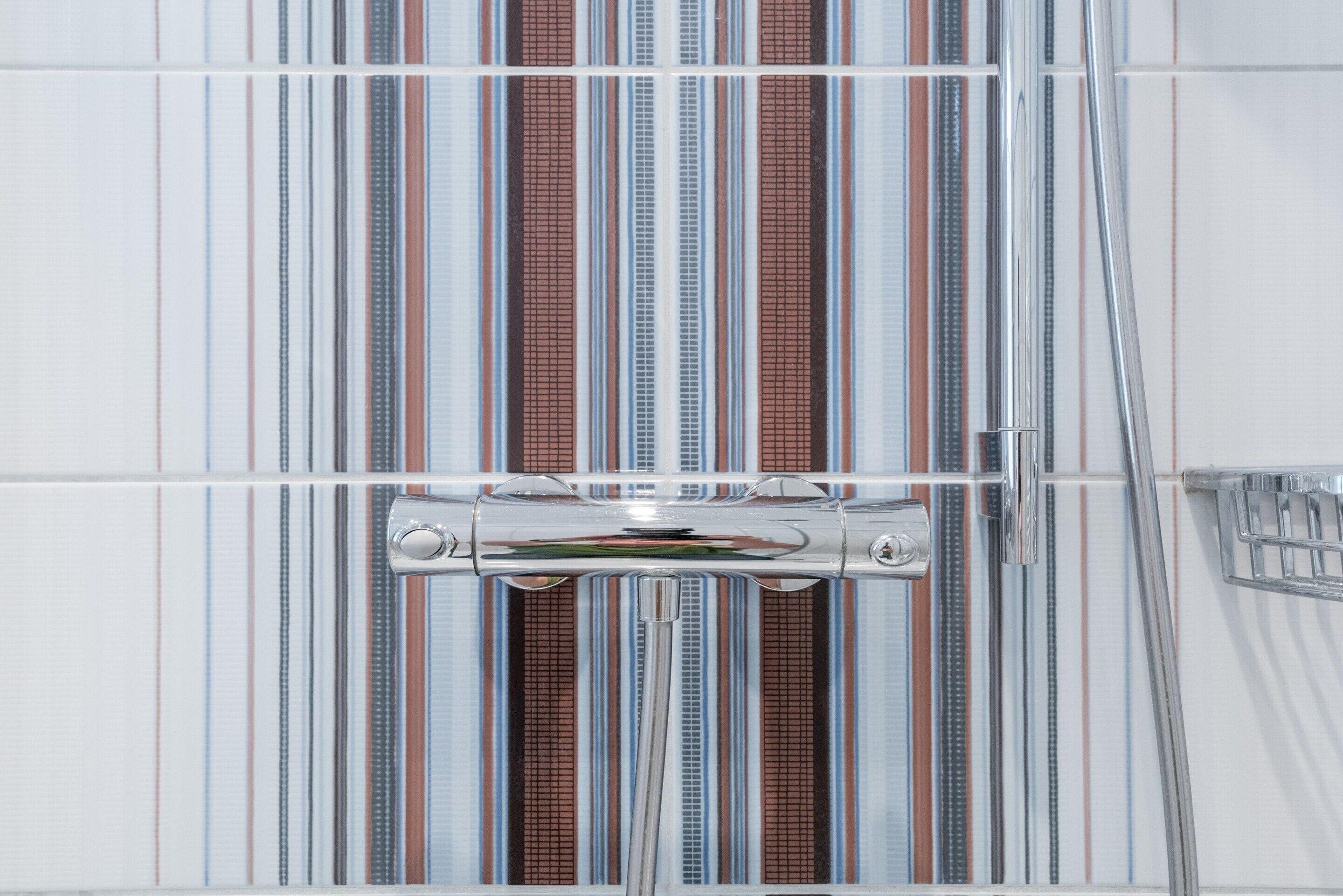 A bathroom with striped tiles, a chrome shower head, and a chrome faucet.