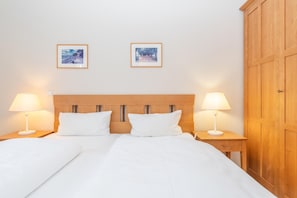 A double bed with white linens, two bedside lamps, a wooden headboard, and two framed pictures on the wall. - Komfortable Ferienwohnung im Seepark Sellin (Sellin)