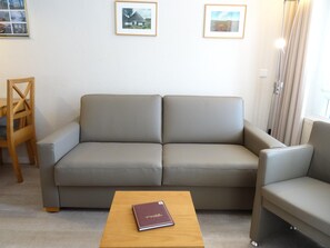A neutral-toned sofa with a wooden coffee table in front, a wooden chair, and two framed pictures on the wall. - Komfortable Ferienwohnung im Seepark Sellin (Sellin)